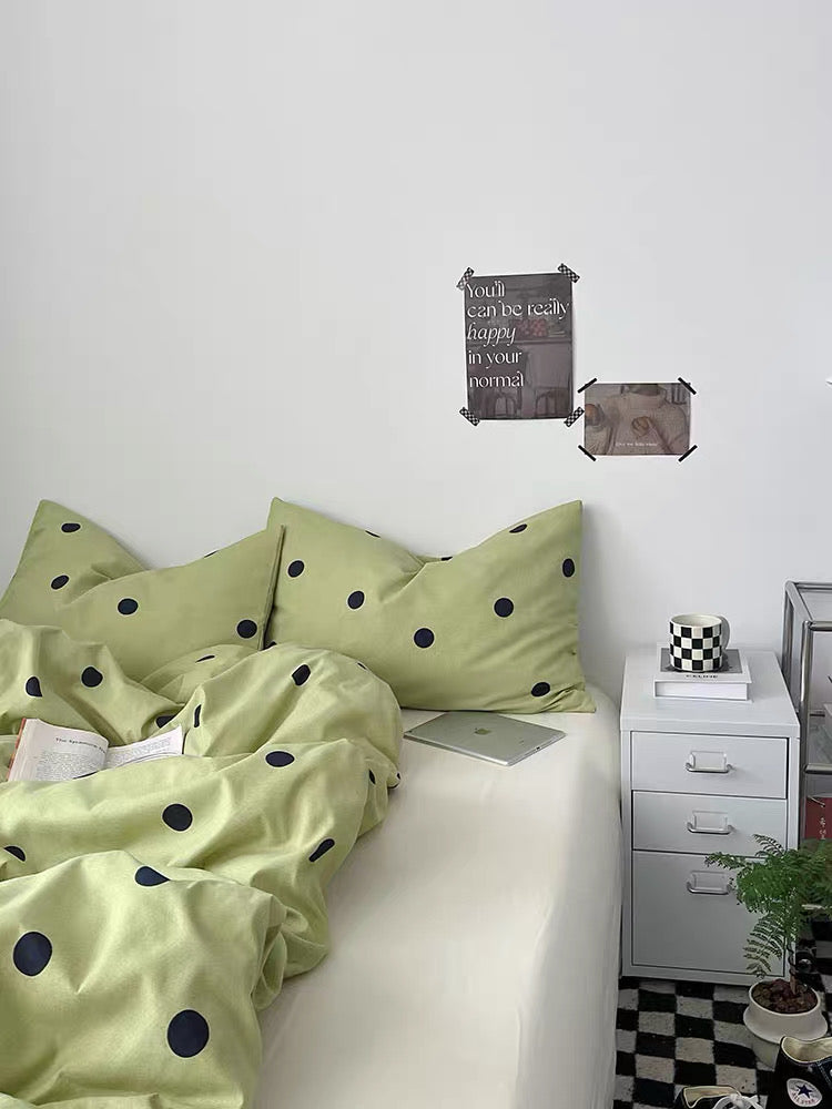 Bed with green polka dot bedding and a white nightstand in a room.