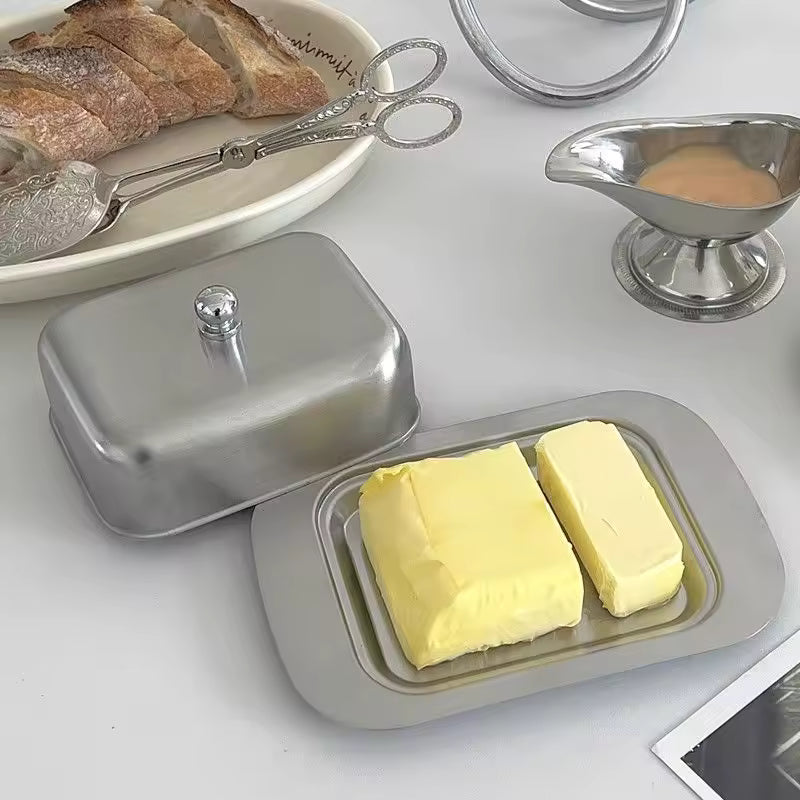 Silver butter dishes on a table with toast, candle, and bottle of wine.