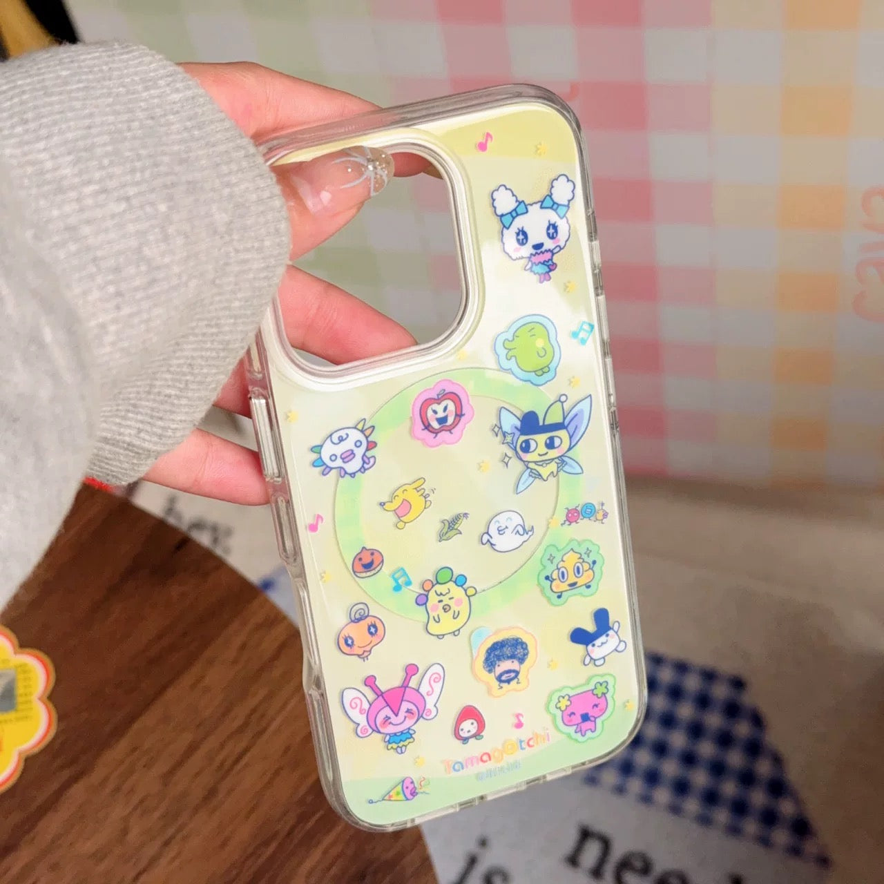 Phone case with colorful cartoon designs held by a person against a checkered background