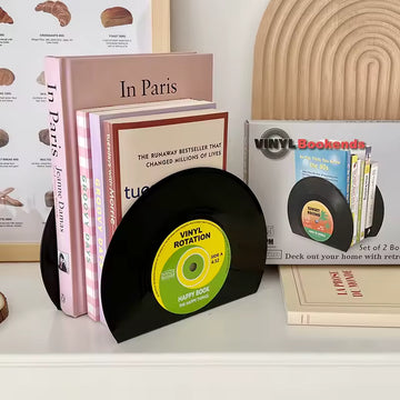Vinyl record bookends holding books on a shelf with a decorative wall in the background.