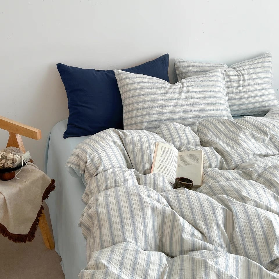 Rumpled seafoam blue duvet cover and striped pillowcases piled together on a cozy unmade bed