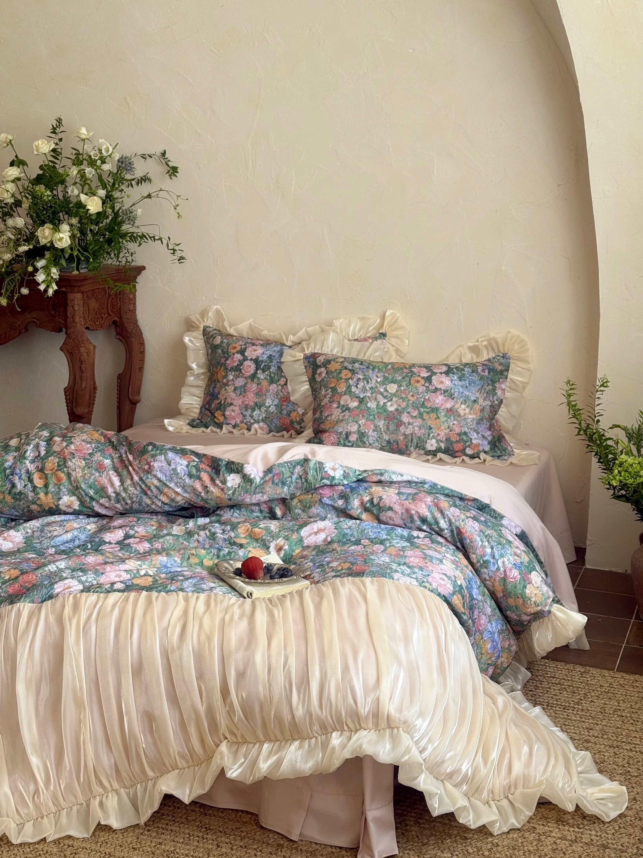 Floral bedding set on a bed with decorative pillows and a side table with flowers.