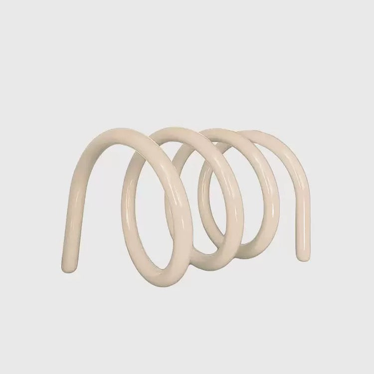 Pink metal bookend holding a green book on a wooden floor with a wire basket in the background.