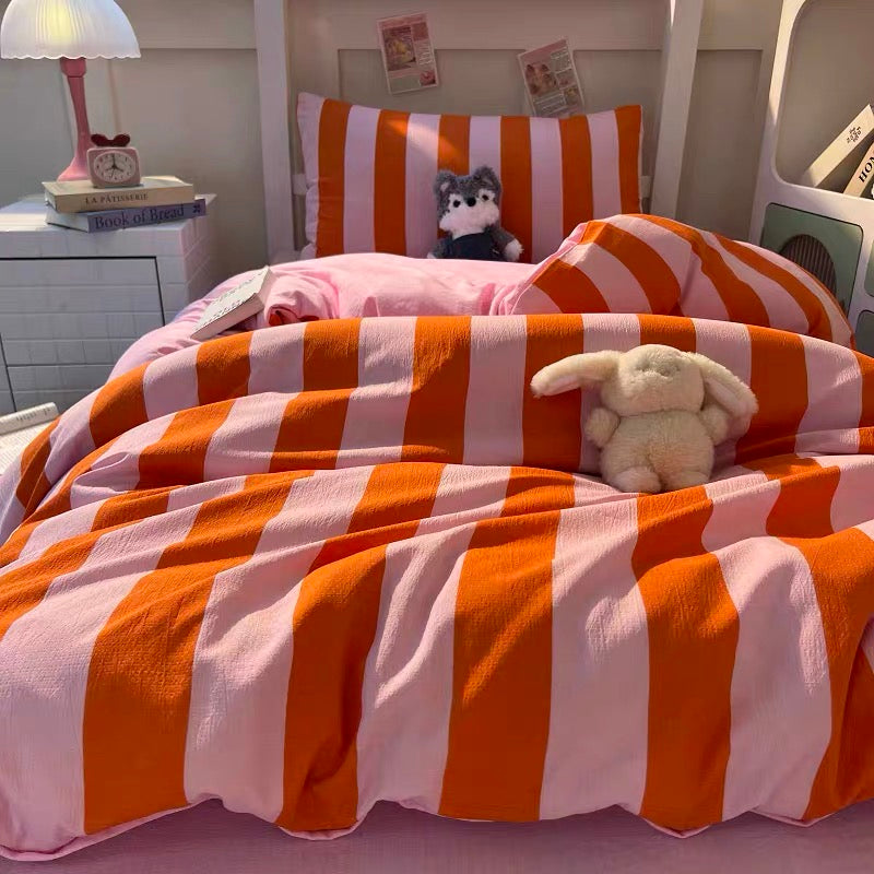 Orange and white striped bedding set on a bed, including a duvet cover and matching pillowcases, styled with a white bunny plush toy, a cup on a saucer, and a bedside lamp.