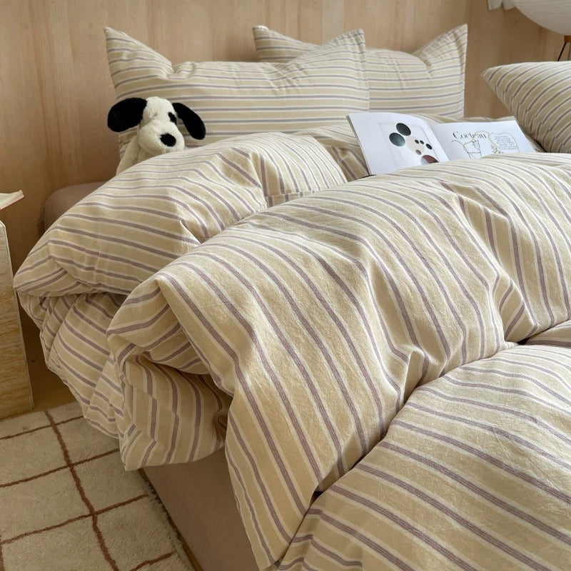 Striped bedding set on a bed with a teddy bear and book in the background.