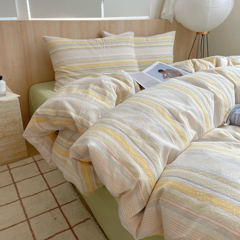 Striped bedding on a bed with a side table and lamp in a room.