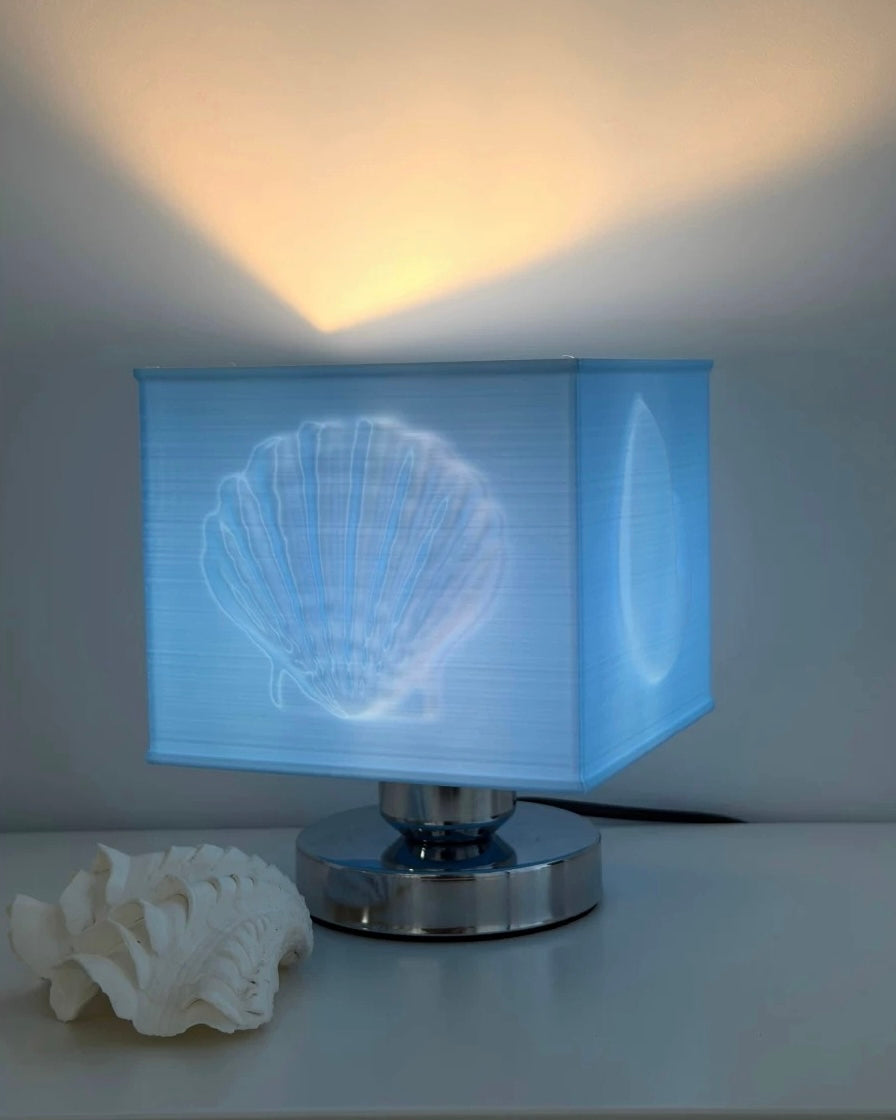 Table lamp with shell design on the shade next to a real shell on a white surface