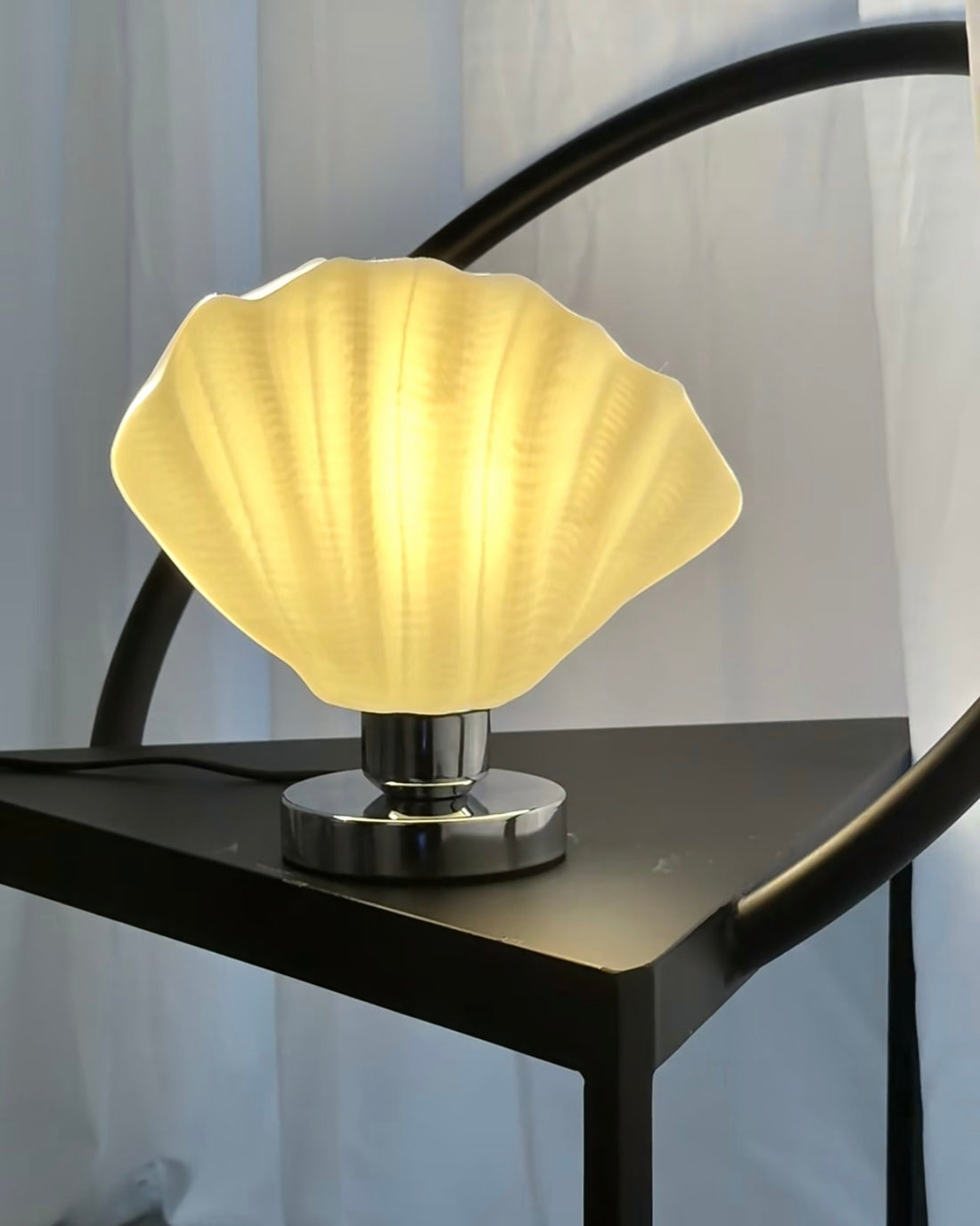 White scallop table lamp with shell relief design on bedside table creating soft warm ambient light