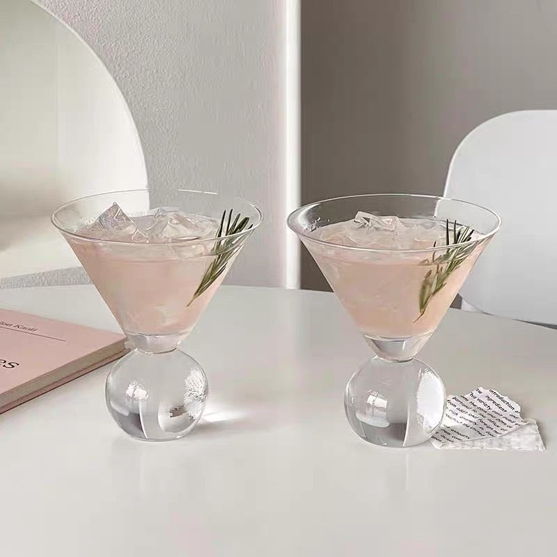 Two pink cocktails with rosemary garnish on a white surface.