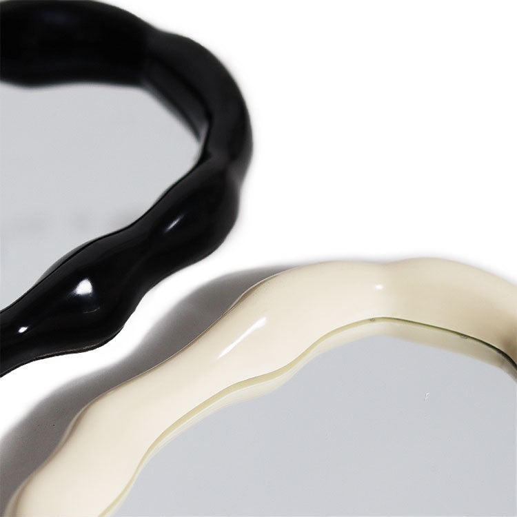 Close-up of two wavy-edged mirrors with glossy black and cream-colored frames on a white background.