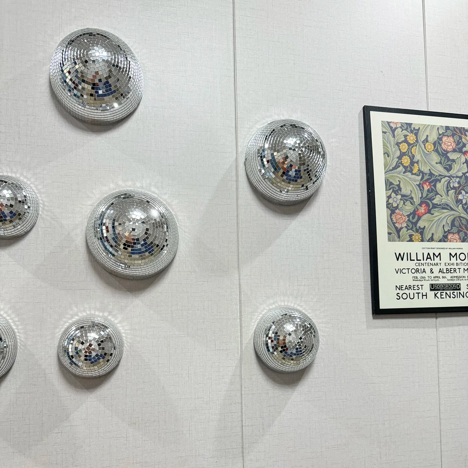 Silver disco balls on a white wall with a framed picture of William Morris art.