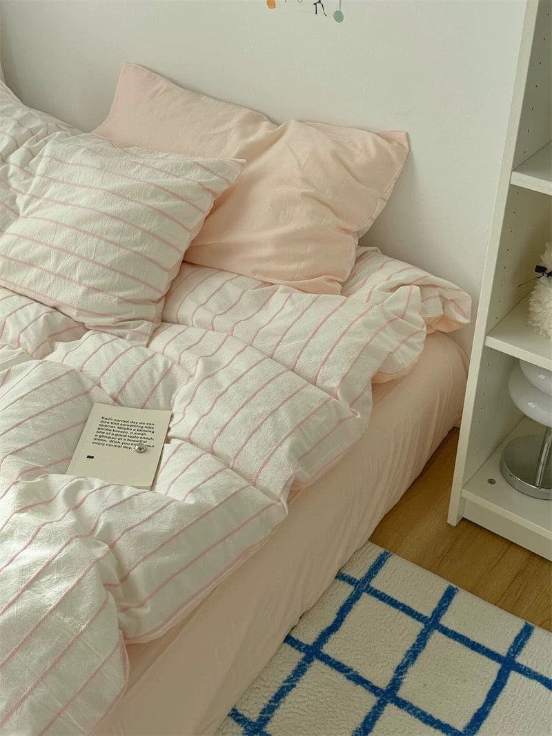 Pink bedding with a white comforter on a bed in a room with a rug and shelf.
