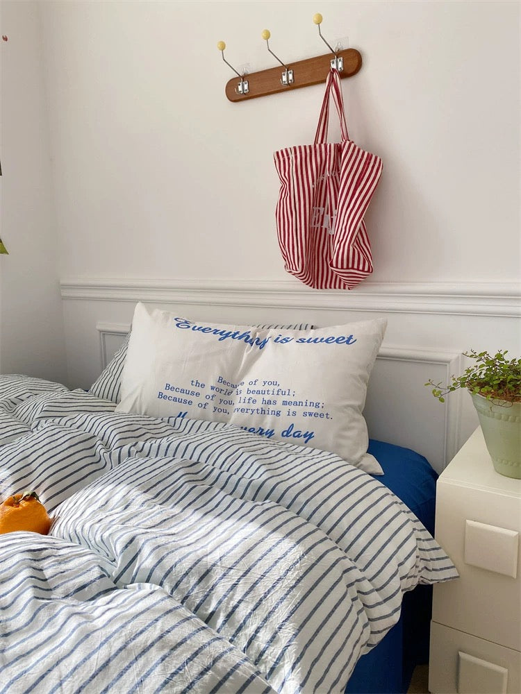 Bedroom with blue bedspread, striped comforter, and decorative pillows.