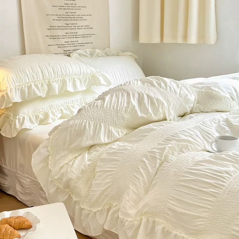 White textured comforter on a bed with pillows and a side table in the foreground.