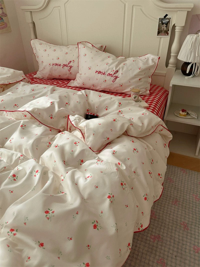 Bedding set with floral pattern and 'rose only' text on a bed with red checkered blanket.