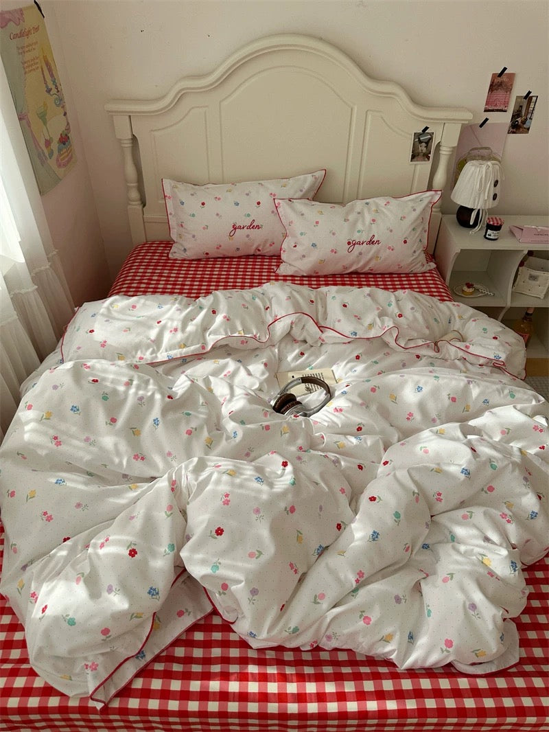 Bed with white floral comforter and red checkered sheets in a bedroom setting.