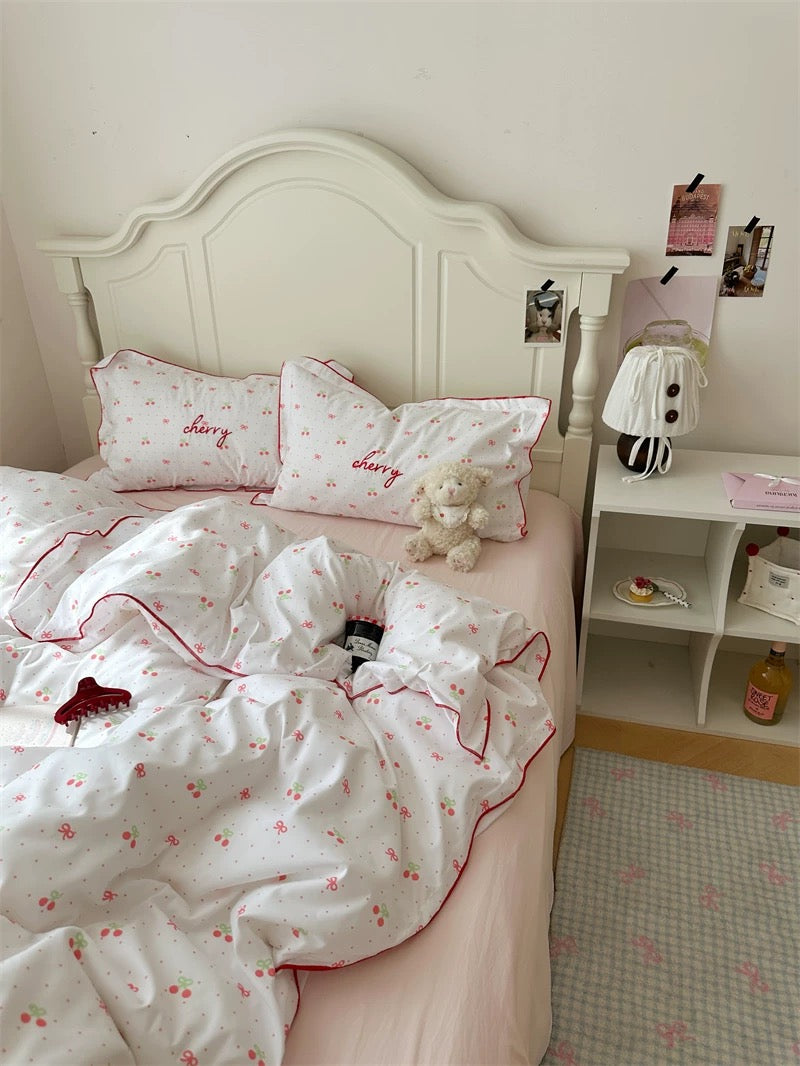 Bedroom with white bedding and pink accents, featuring a teddy bear and small nightstand.