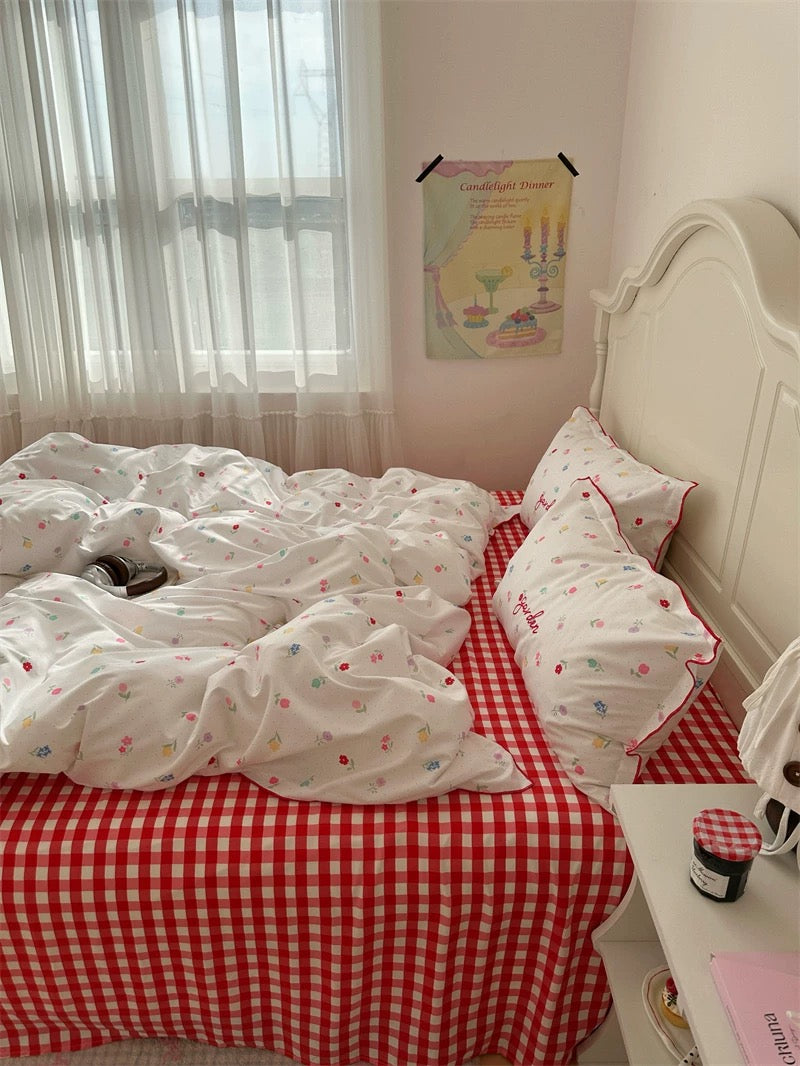 Bed with white bedding and red checkered blanket in a room with a window and poster on the wall.