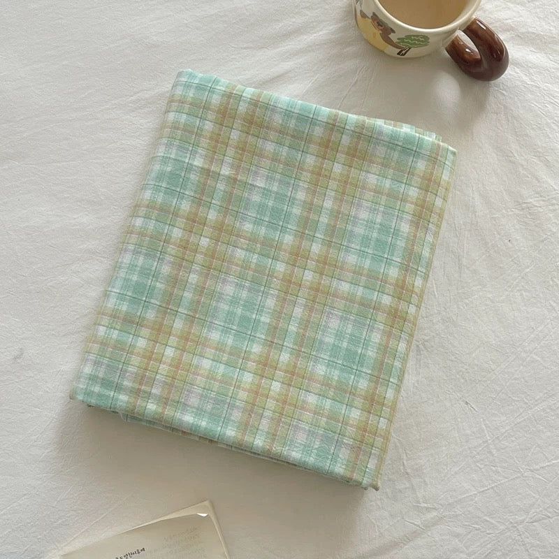 Plaid fabric sample on a textured white surface with a cup in the background