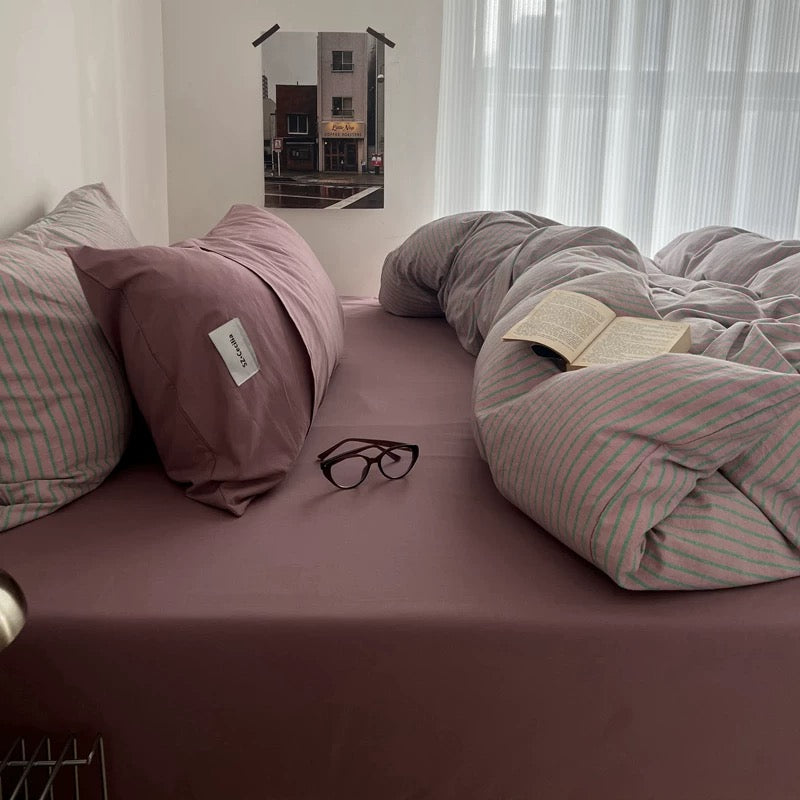 Bed with pink bedding, glasses, and a book in a room with a window and picture frame.