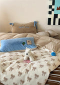 Dog lying on a bed with a patterned blanket, pillows, and a small painting on the wall.