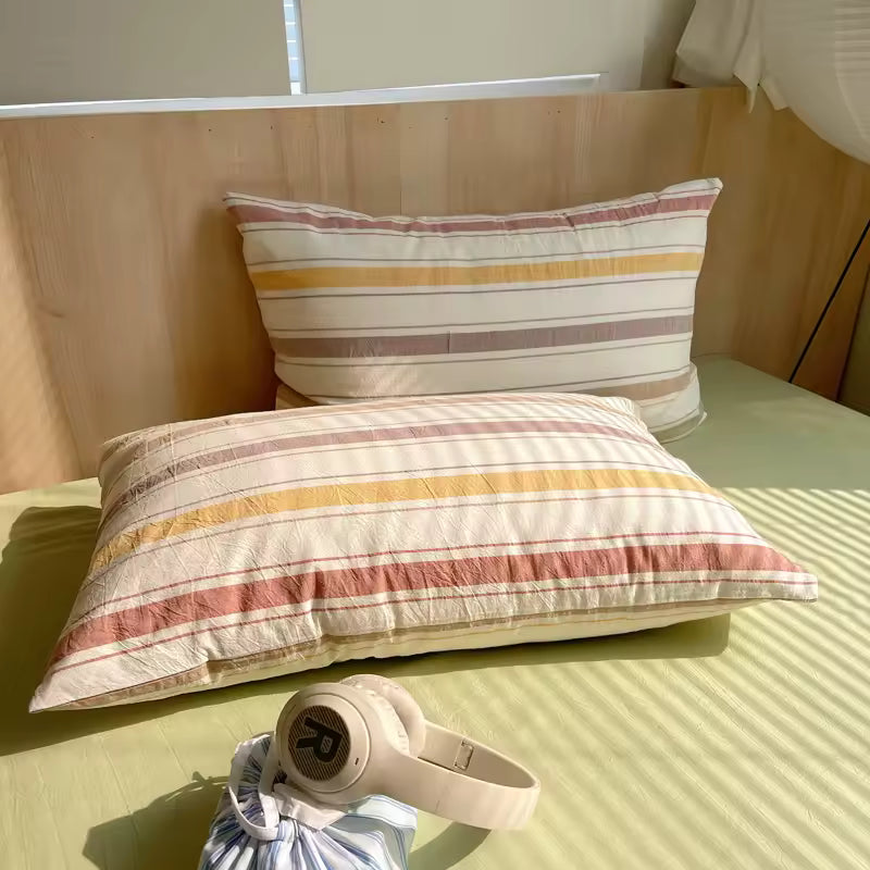 Striped pillows on a bed with a small bag and headphones in the foreground.