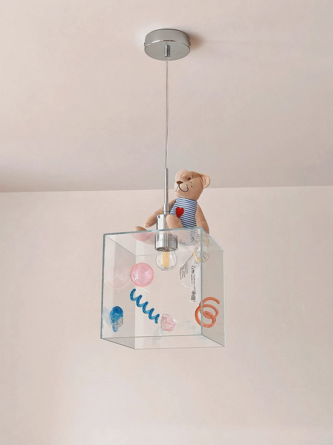 Clear glass pendant light with colorful decorations on a white wall background