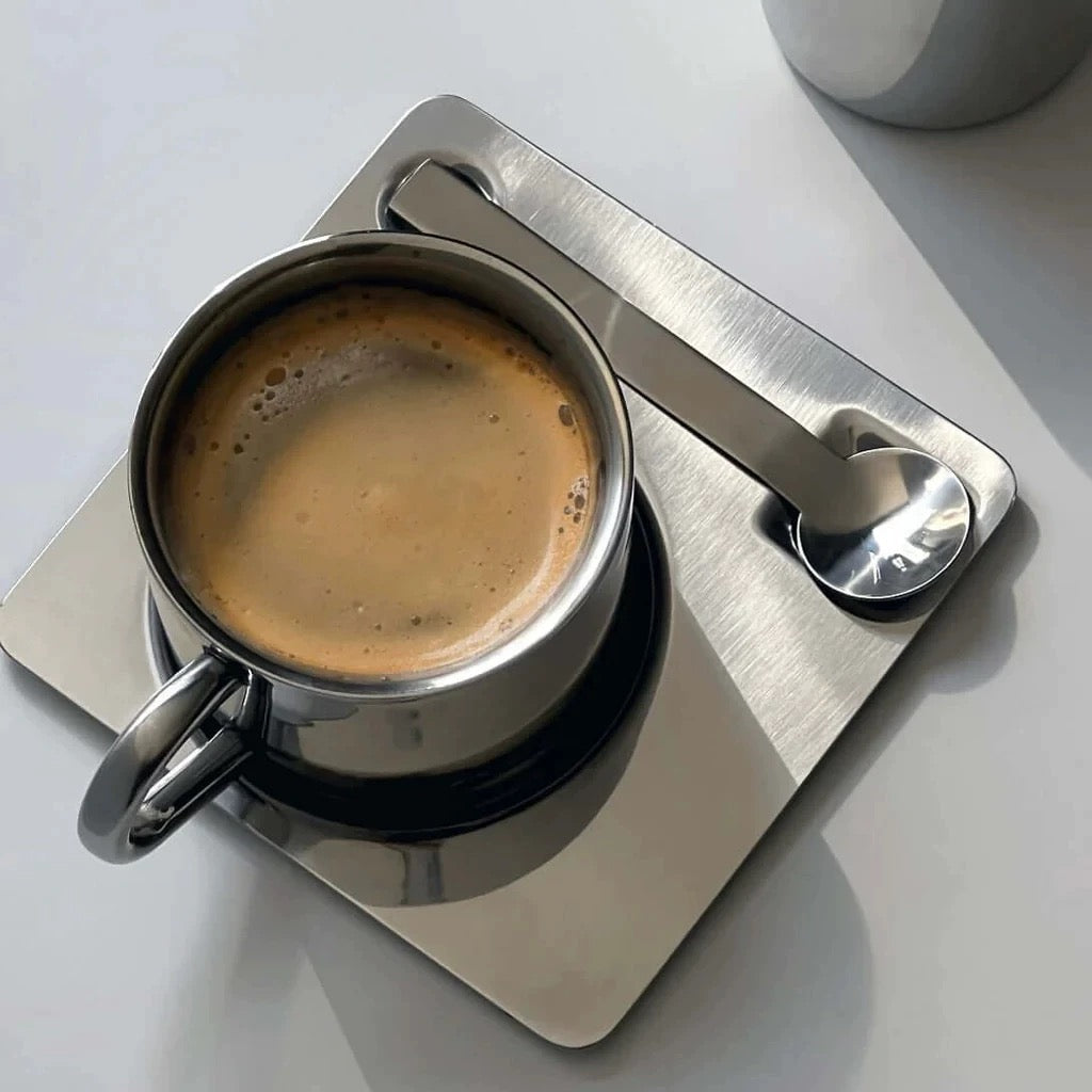 Espresso cup on a metal coaster with a spoon on a white surface