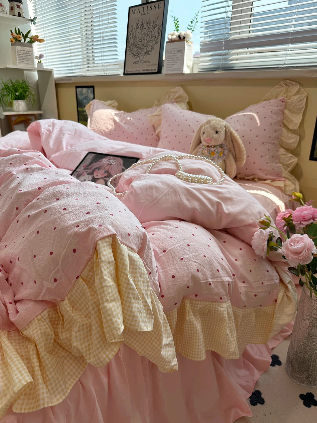 Pink and white polka dot comforter on a bed with pillows and a teddy bear.