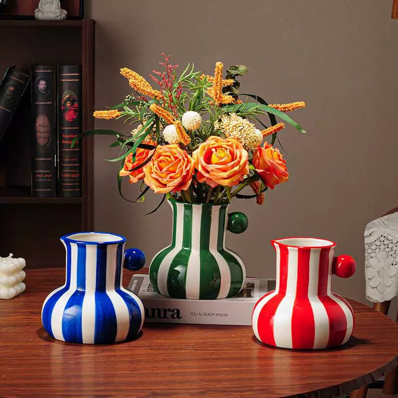 Set of colorful striped vases on a wooden table with a hand holding a yellow and white striped vase.