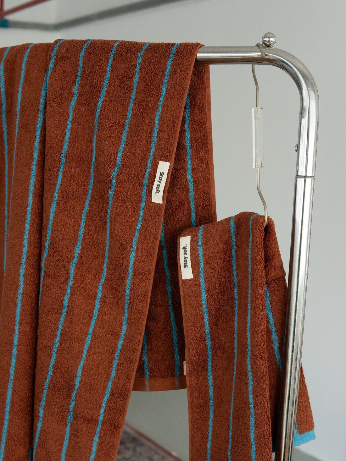 A stack of brown cotton towels with turquoise stripes, featuring a white pump bottle of hand wash and a small white brand tag reading 'sopapal' on a wooden tray.