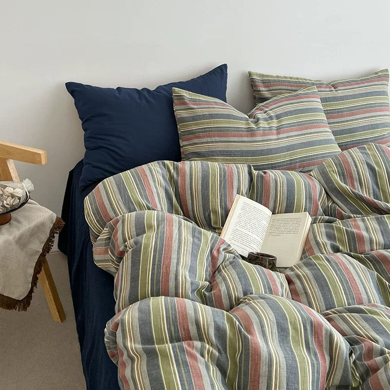 A bed dressed in a striped duvet cover and matching pillowcases with blue pillows, styled in a bedroom setting with a book on the duvet.