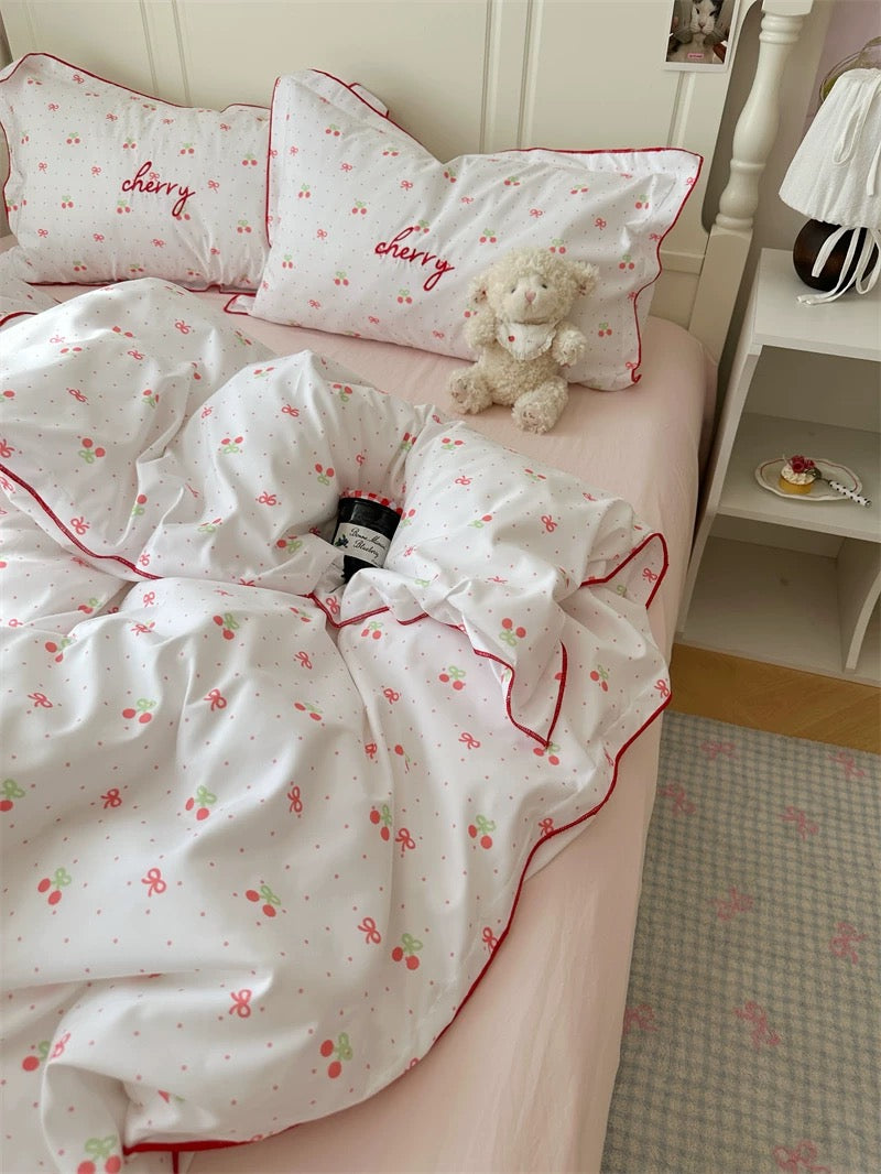 Bed with cherry-themed bedding and a teddy bear, in a room setting.