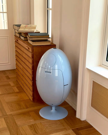 White egg-shaped device on a wooden floor next to a stack of books.
