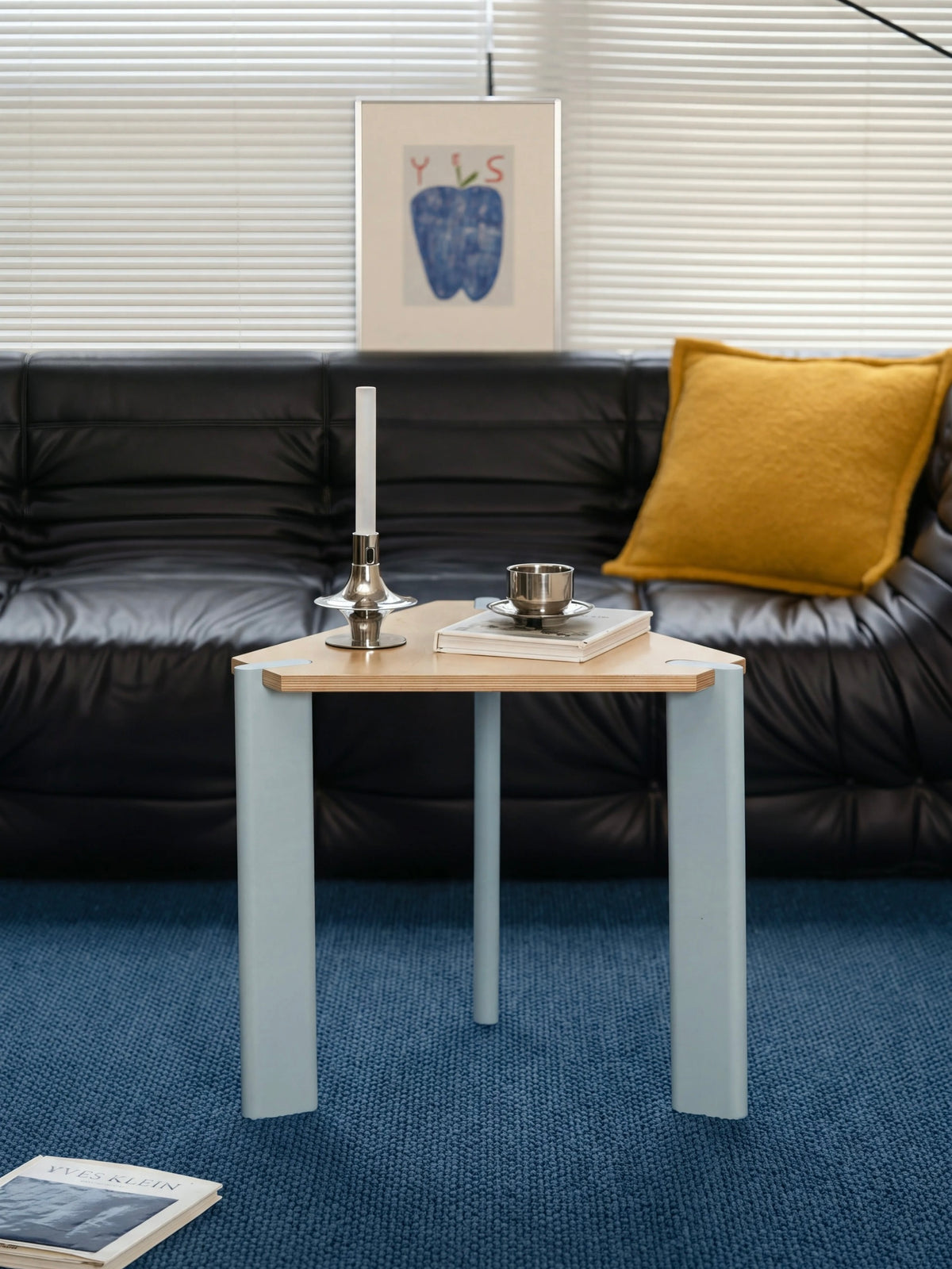 Triangular side table seen from the front with three pale legs, a wood top and small objects on the surface.