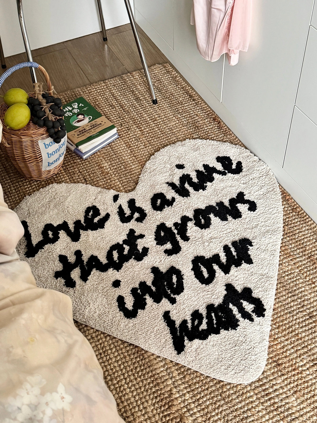 Cream heart typography rug with black script lies beside a bed, its rounded top and pointed base fully visible.