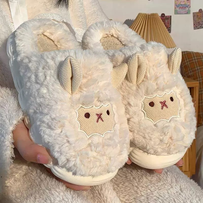 Pair of fluffy white slippers with animal face design held by a person.