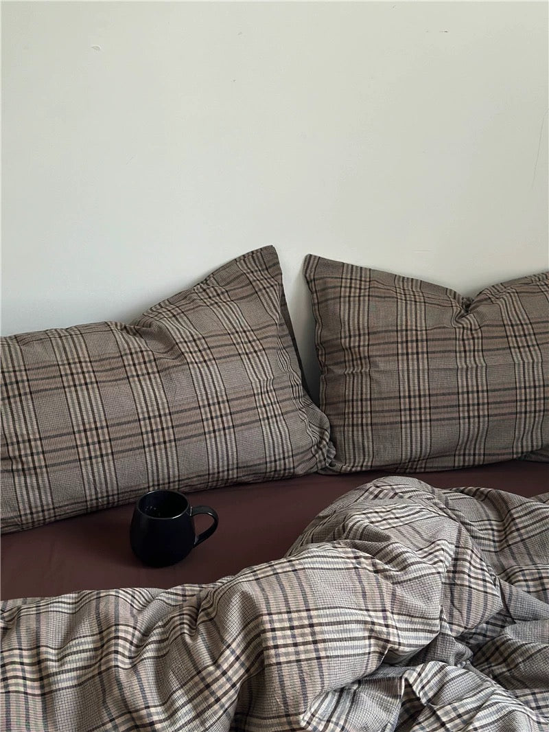 Plaid pillows and blanket on a bed with a cup on the nightstand.