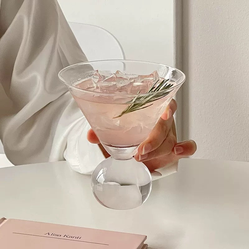 Hand holding a pink cocktail with ice and a rosemary sprig in a clear glass.