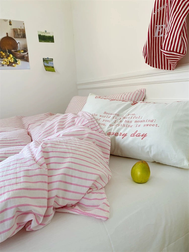 Bed with pink and white striped bedding and pillows, with a green apple on the bed.