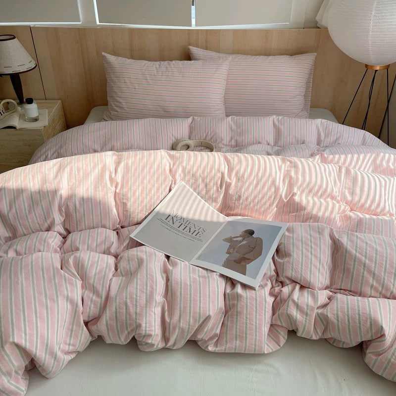 Bed with pink striped bedding and a magazine on top, in a bedroom setting.