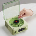 Green record player with a hand placing a record on it, on a white surface.