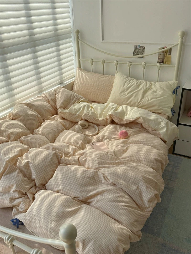 Unmade bed with beige bedding in a room with a window and white walls.