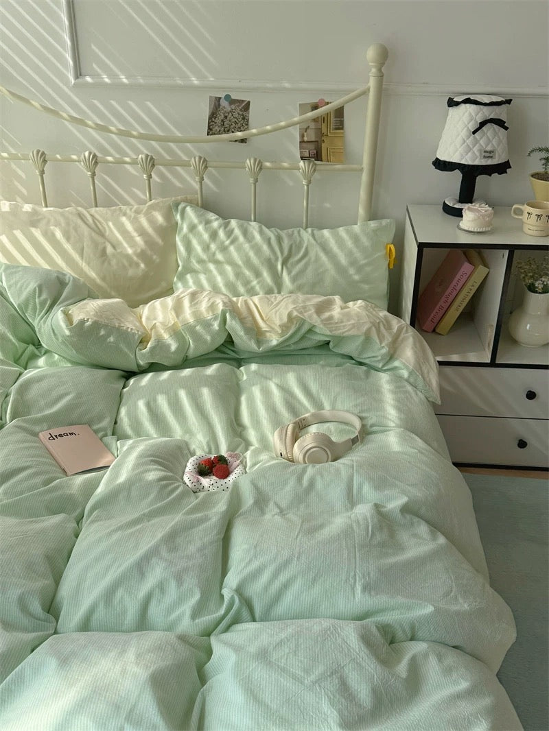 Light green comforter on a bed with a white nightstand and decor items in a bedroom.