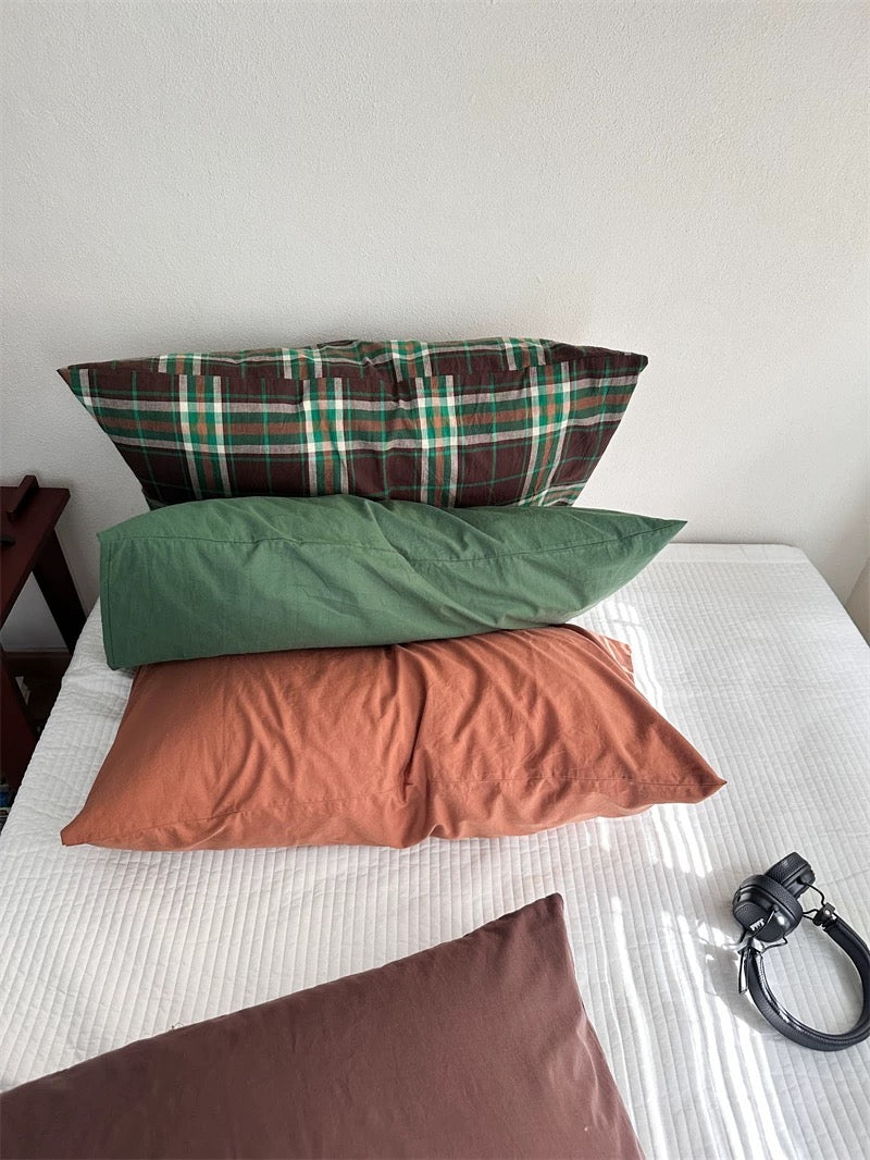 Brown and green plaid pillowcases rest above solid green and rust orange designs.