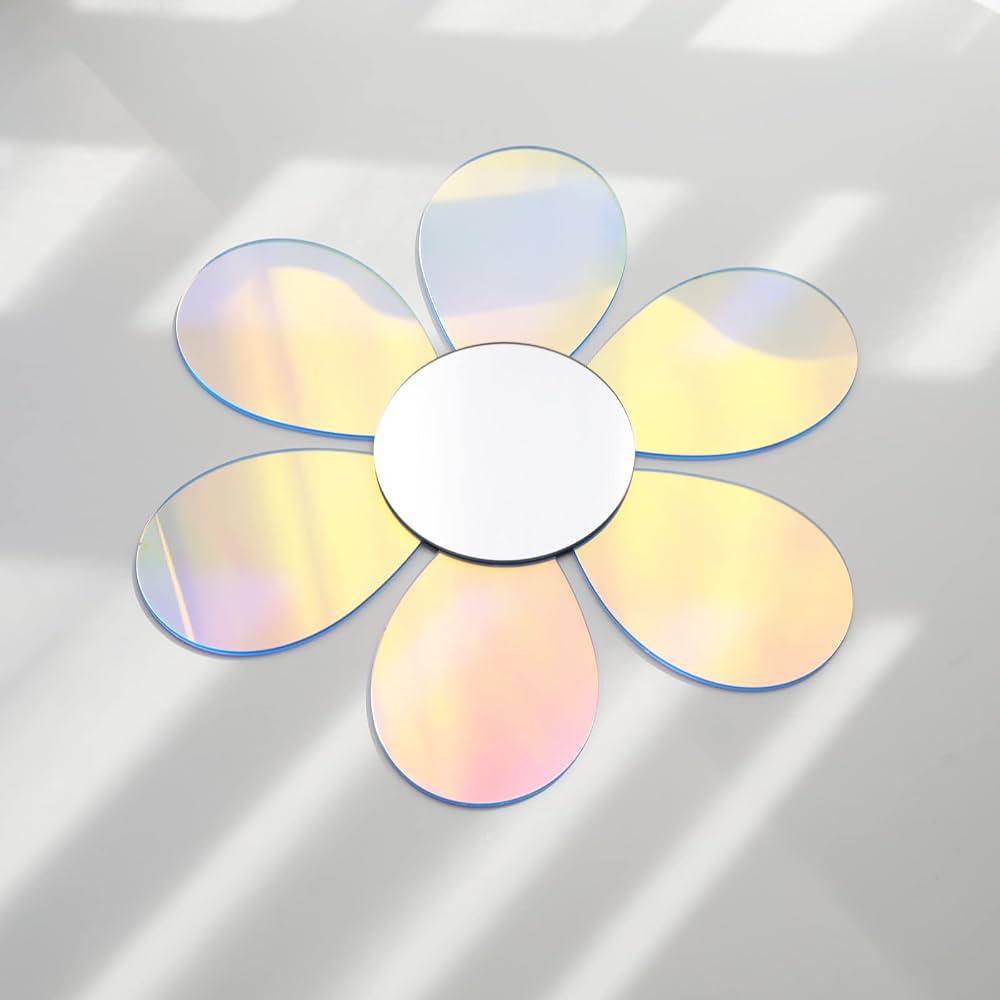 A flower-shaped decorative mirror with six iridescent petals and a white circular center, photographed on a light gray surface with soft window-shadow lighting.