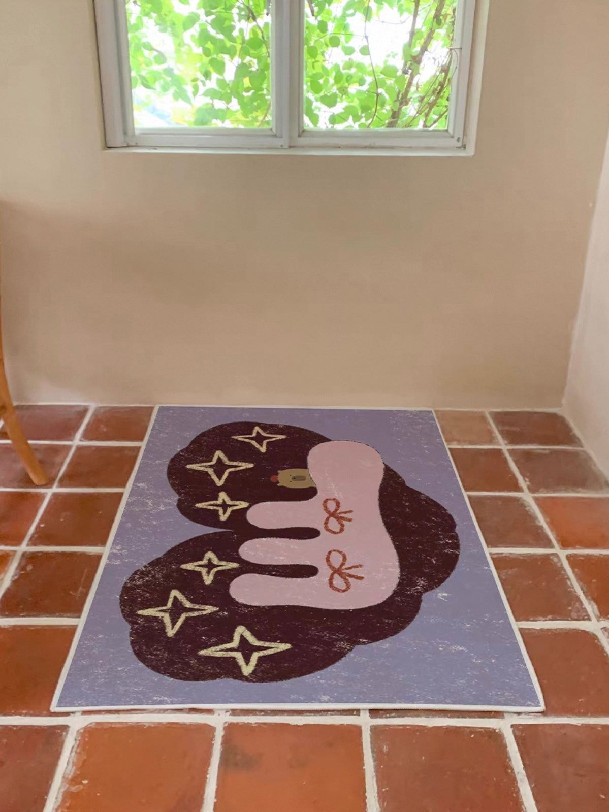 A whimsical rug with pink bows and pale stars on a purple base lies flat beneath a window.