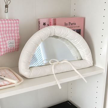 White bow mirror with a padded semicircular frame and matching ribbon, leaning against a dark background.