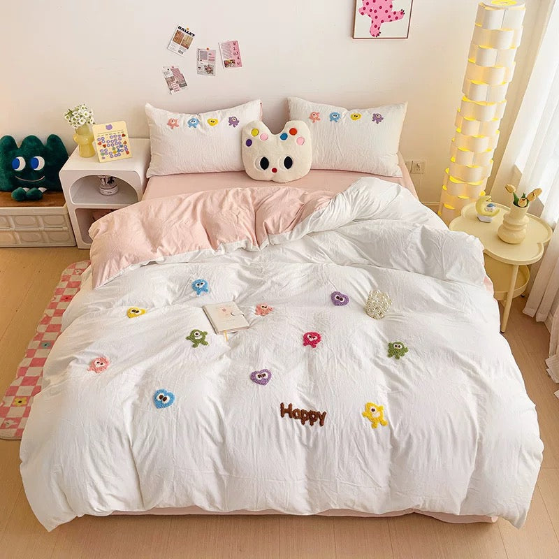 Wide bedroom view of white cartoon embroidered bedding with pink layers and matching character pillowcases.