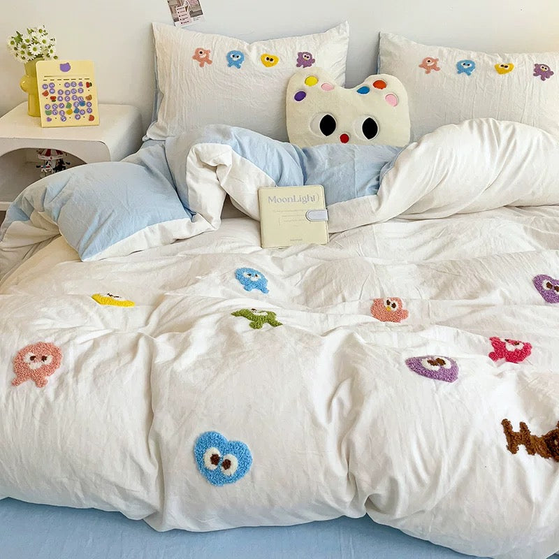 White embroidered duvet with colorful cartoon figures layered over light blue bedding and matching pillowcases.